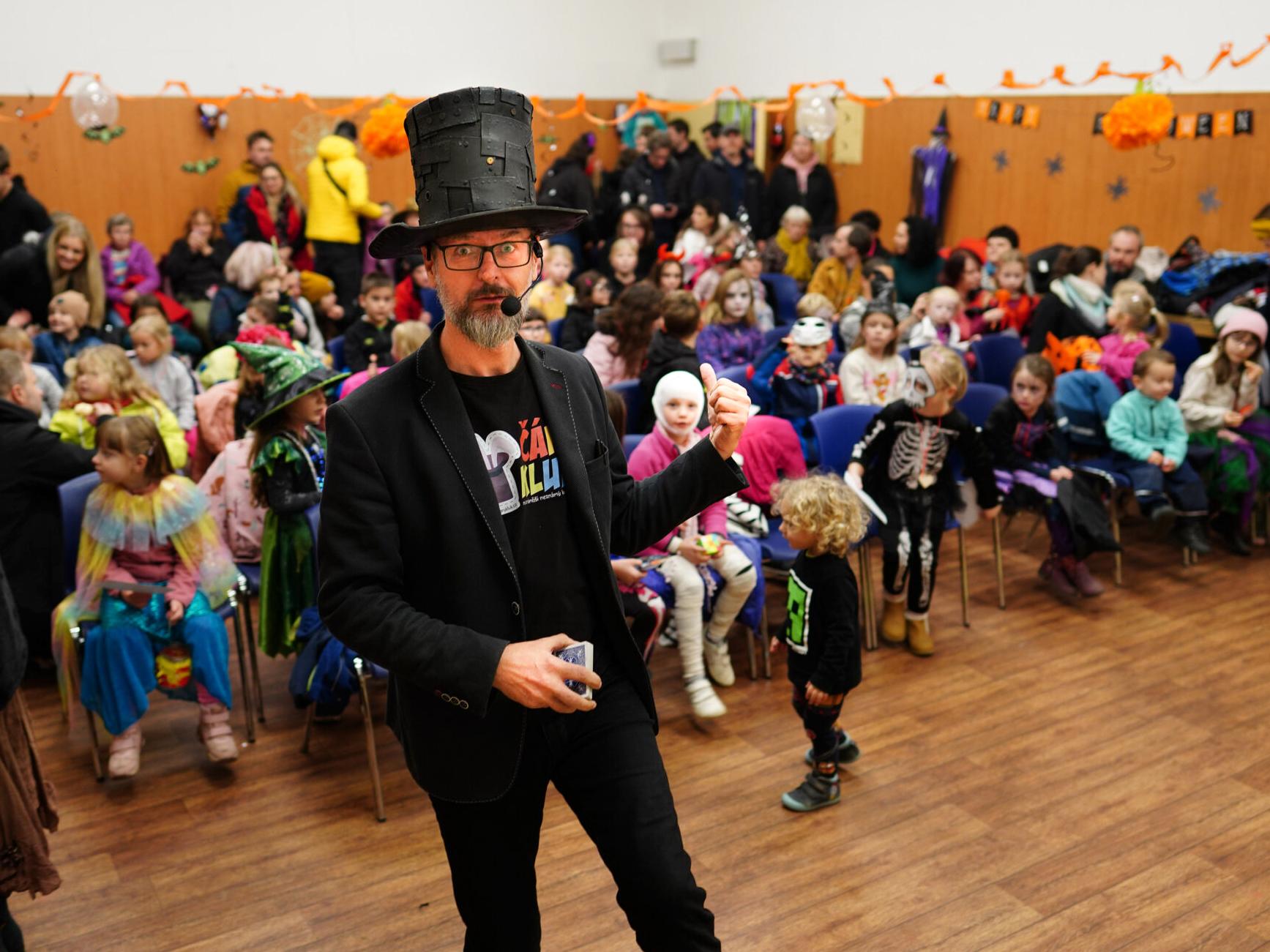 Děti v kostýmech na oslavě. Kouzelník v klobouku s kartami.